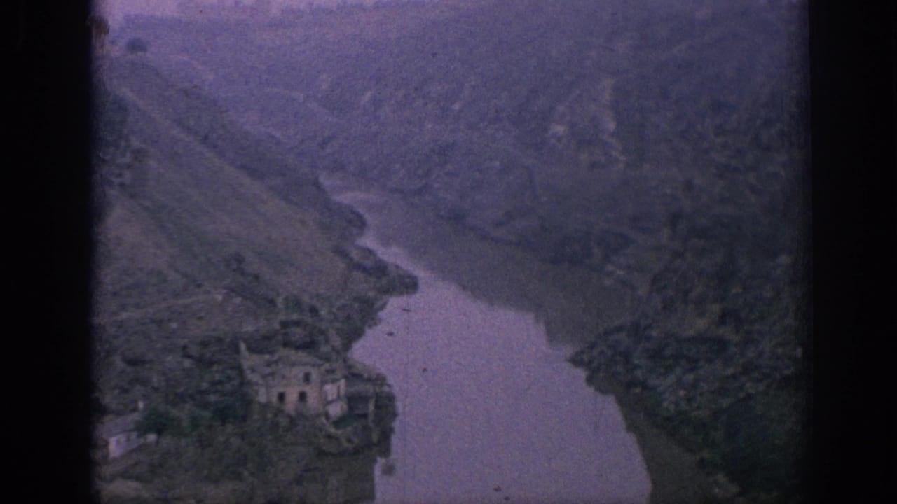 1966 Spain 8mm frame with a winding river, sloped valley walls, and a pale building near the riverbank.