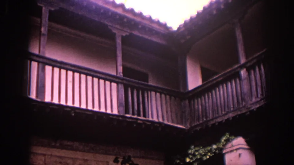 1966 Spain 8mm frame showing a traditional courtyard facade with wooden balcony rails, plaster walls, and a bright opening above.