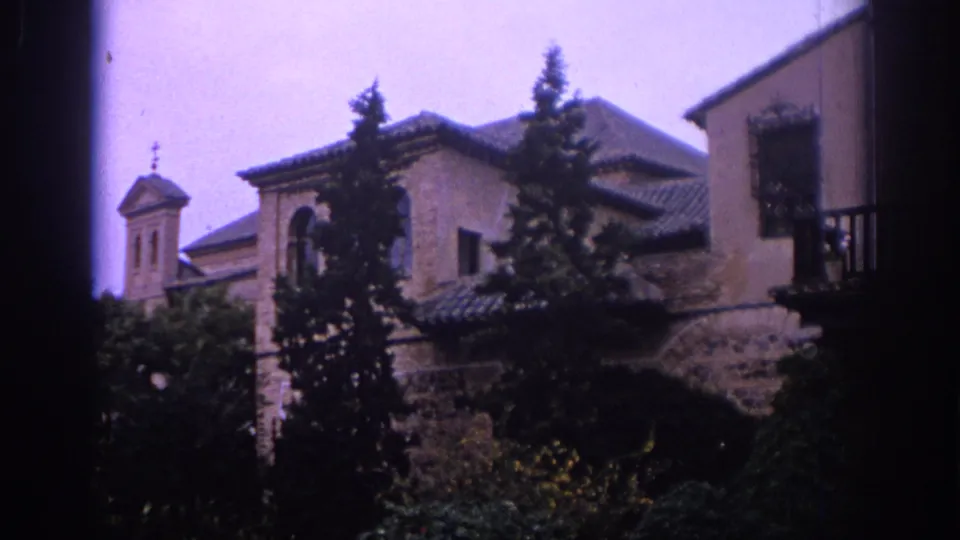 1966 Spain exterior frame showing a traditional building with tiled roofs, trees, balcony detail, and a small church-like steeple in the background.