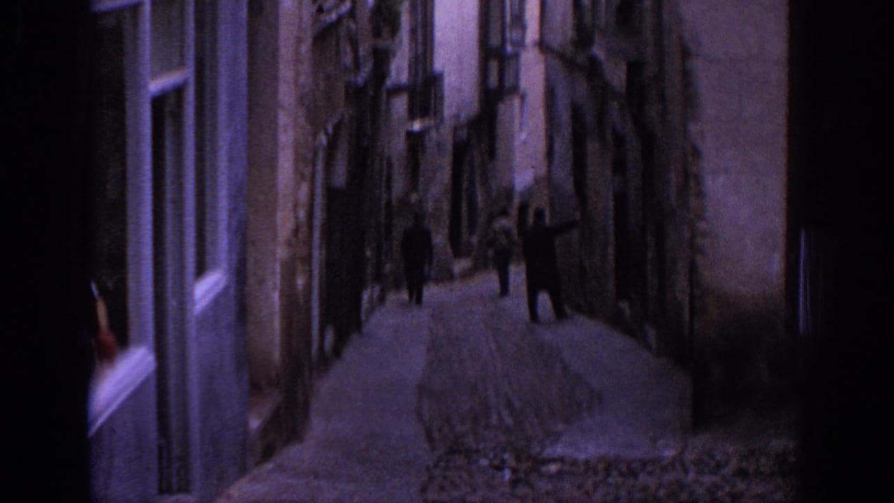 1966 Spain home-movie view down a narrow cobblestone alley lined with old buildings and small figures walking away.