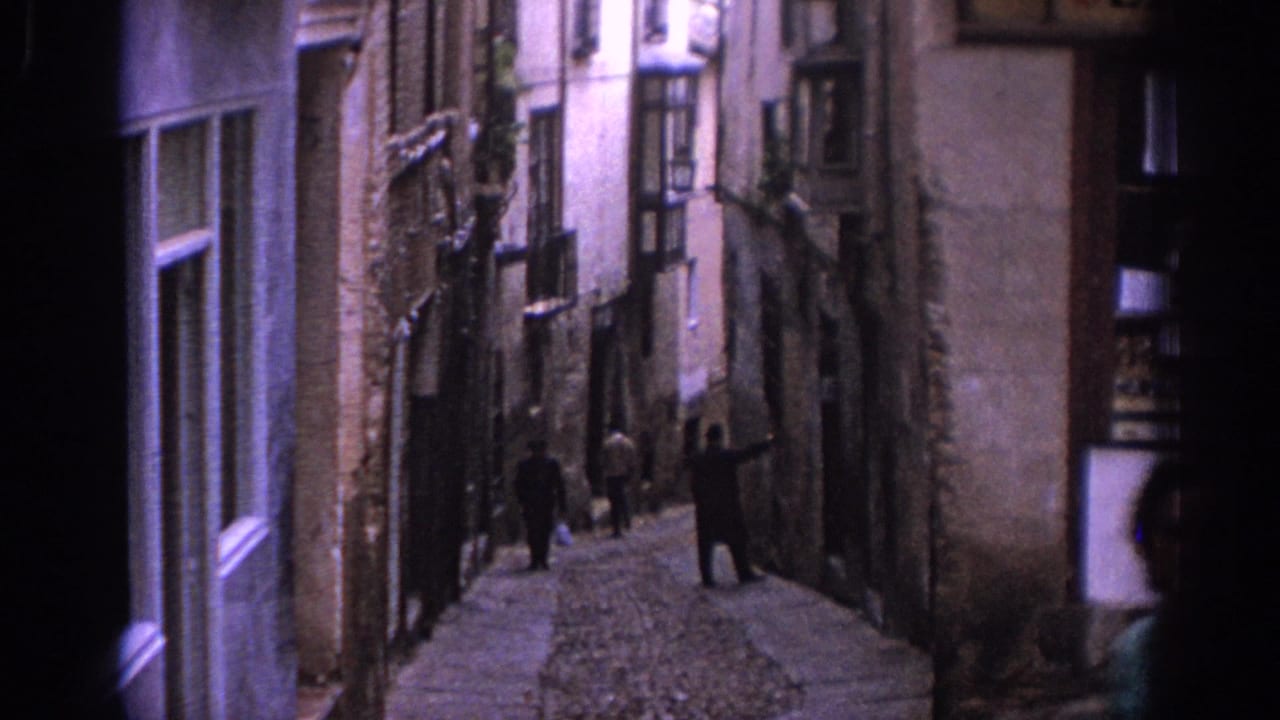 Narrow Spanish alley in 1966 with old facades, balconies and pedestrians walking through the cobbled passage.
