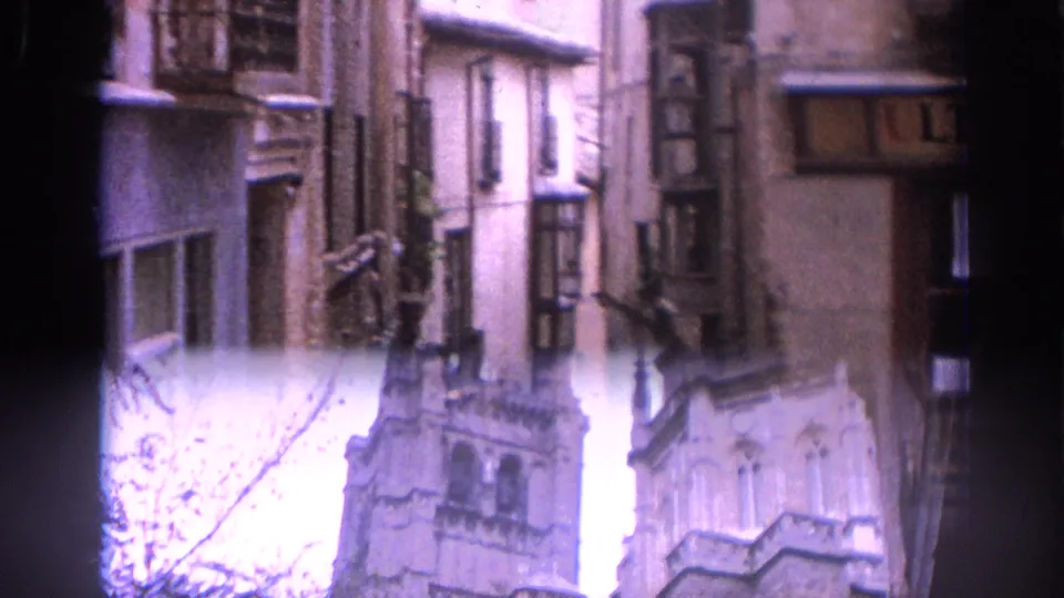The clip ends on Gothic-style cathedral stonework rising beyond historic Spanish street facades in a pale, overexposed sky.