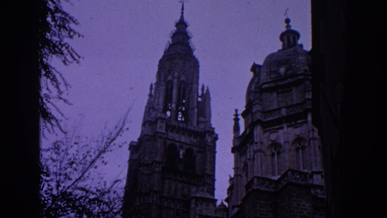 1966 Spain frame with a tall Gothic tower, adjacent domed roof feature, bare branches, and dark foreground tree trunks.