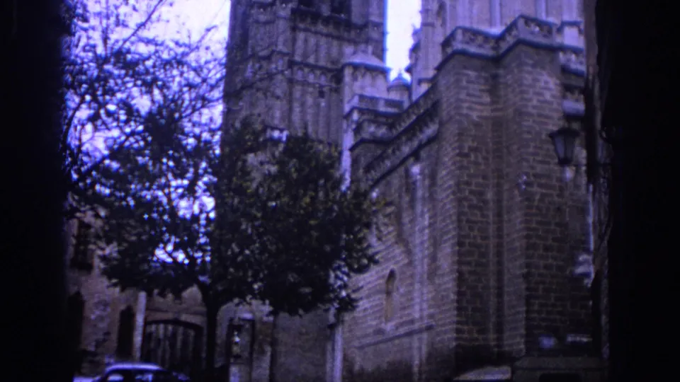 1966 Spain frame showing cathedral stonework, a Gothic tower, roofline detail, tree branches, and soft 8mm color shift.