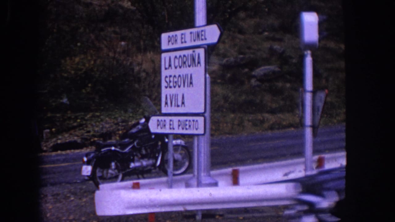 Spanish road signpost beside a parked motorcycle as a bus passes.