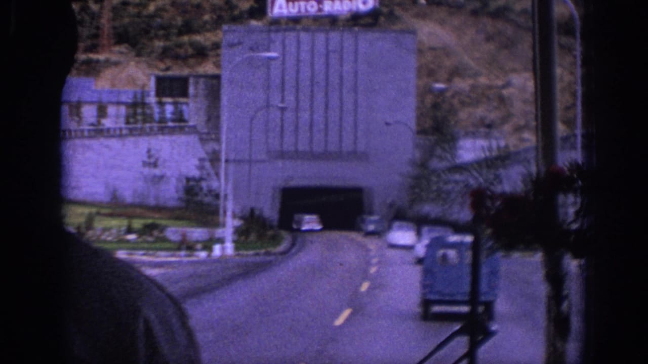 View from inside a vehicle approaching a road tunnel with cars and a small blue truck ahead.