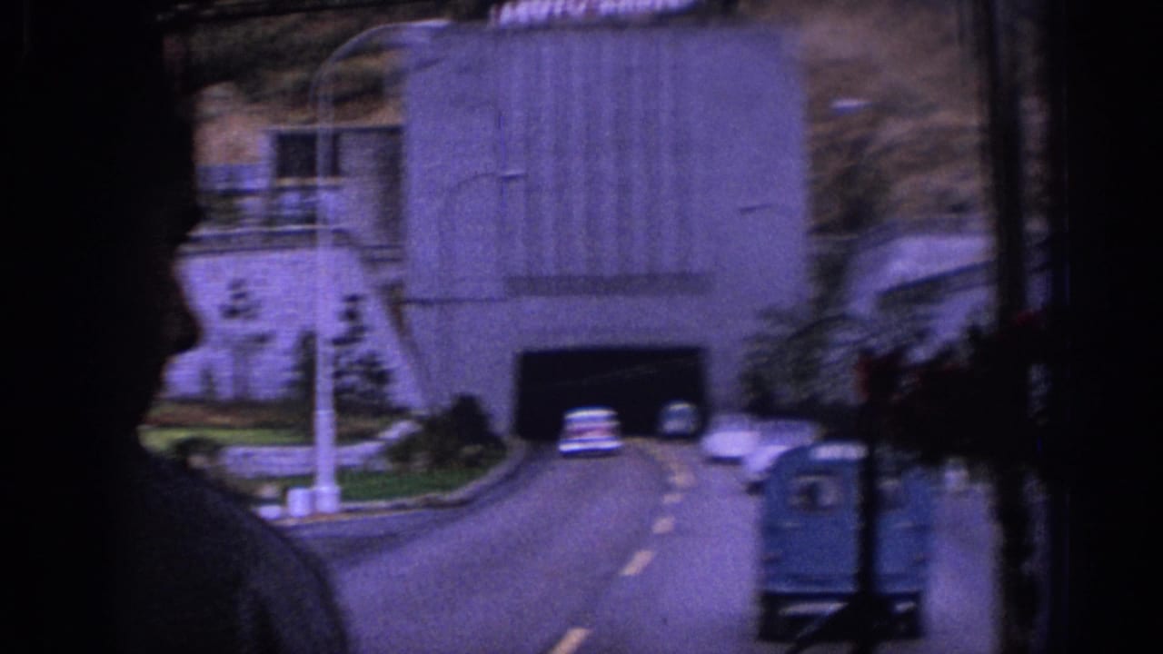 1966 Spain travel footage shows a road leading into a tunnel, with classic cars, a small blue truck, and dark vehicle-window silhouettes framing the view.