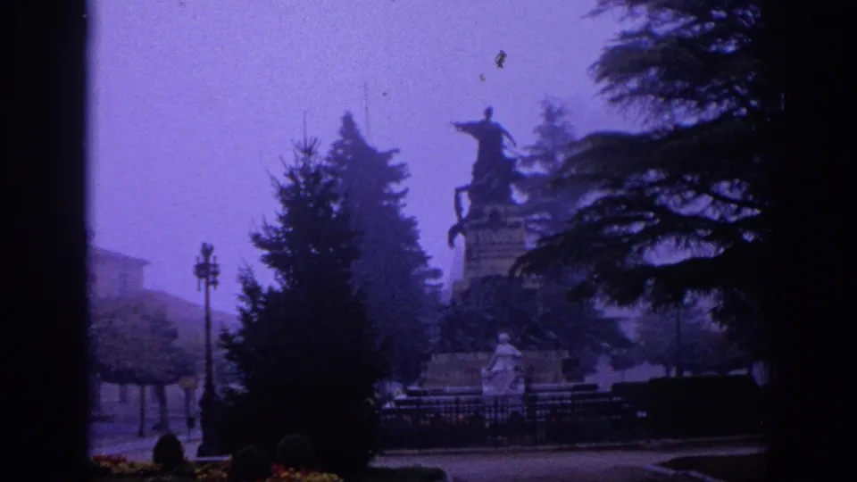 1966 Spain 8mm frame with an equestrian monument partly obscured by evergreens, haze, and dark film-edge shadows.