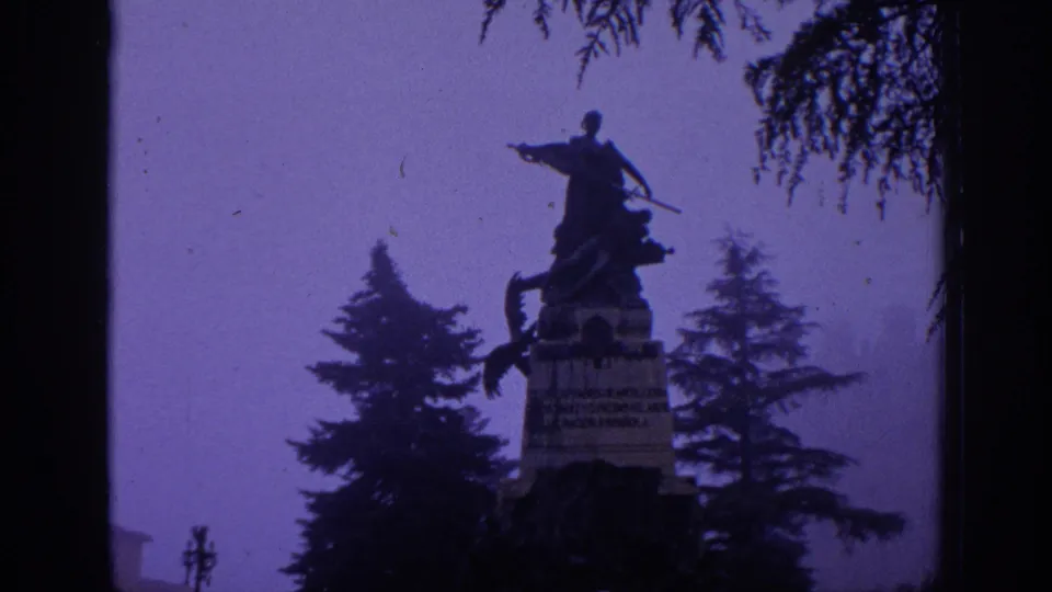 1966 Spain 8mm frame with a closer view of an equestrian statue and pedestal surrounded by dark trees and purple atmospheric haze.