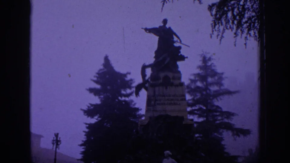 1966 Spain 8mm frame showing a dark equestrian monument above trees, with soft focus and purple color shift.