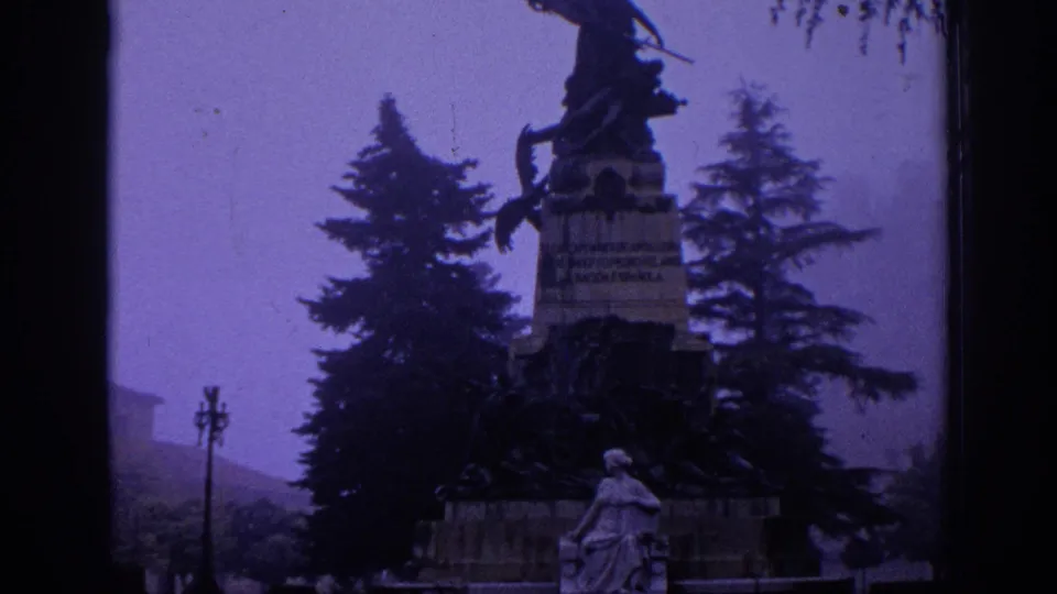 1966 Spain 8mm view of a public monument with an equestrian figure, stone base, trees, and a seated statue below.