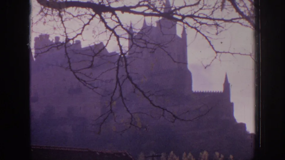 1966 Spain 8mm frame showing a distant castle and pointed tower, with bare branches layered across the foreground.