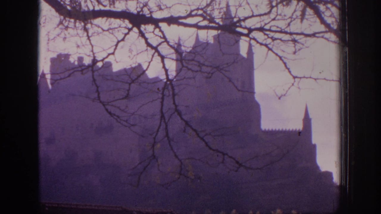 1966 Spain 8mm frame showing a turreted castle silhouette behind bare branches under a faded purple twilight sky.