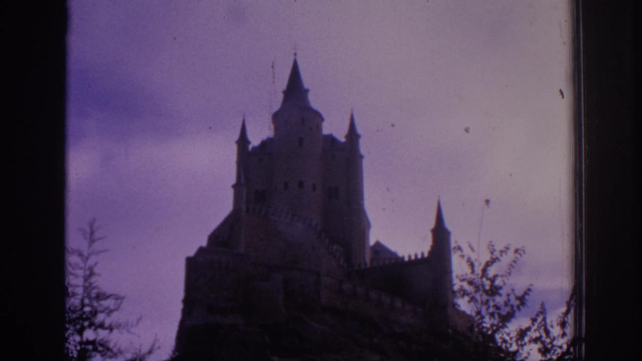 1966 Spain 8mm frame with a turreted castle seen from below, its battlements and rocky base in dark silhouette.