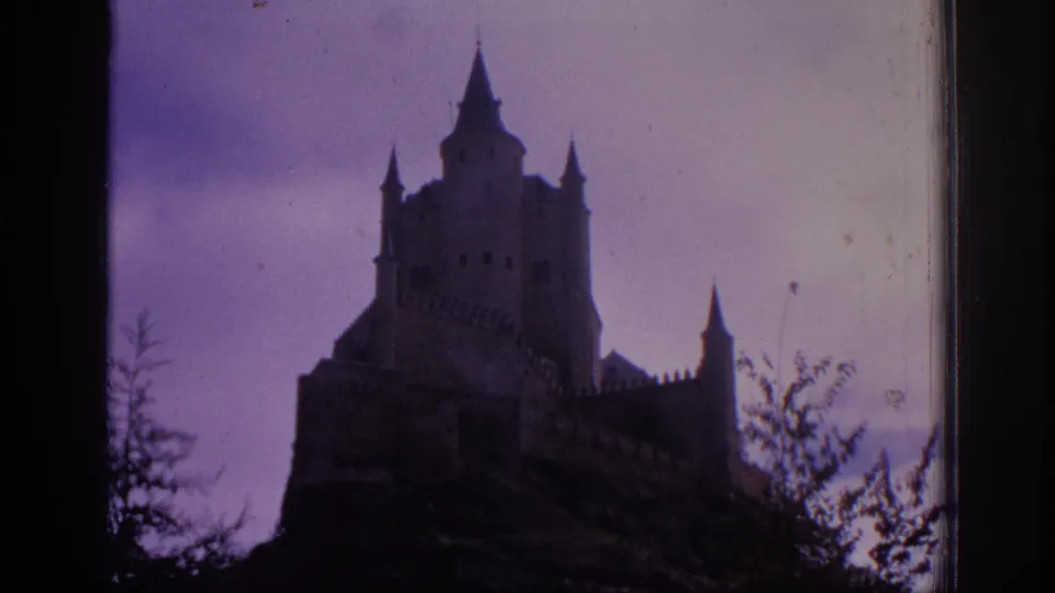 1966 Spain 8mm frame showing a soft, grainy low-angle view of a castle with pointed towers and silhouetted foliage.