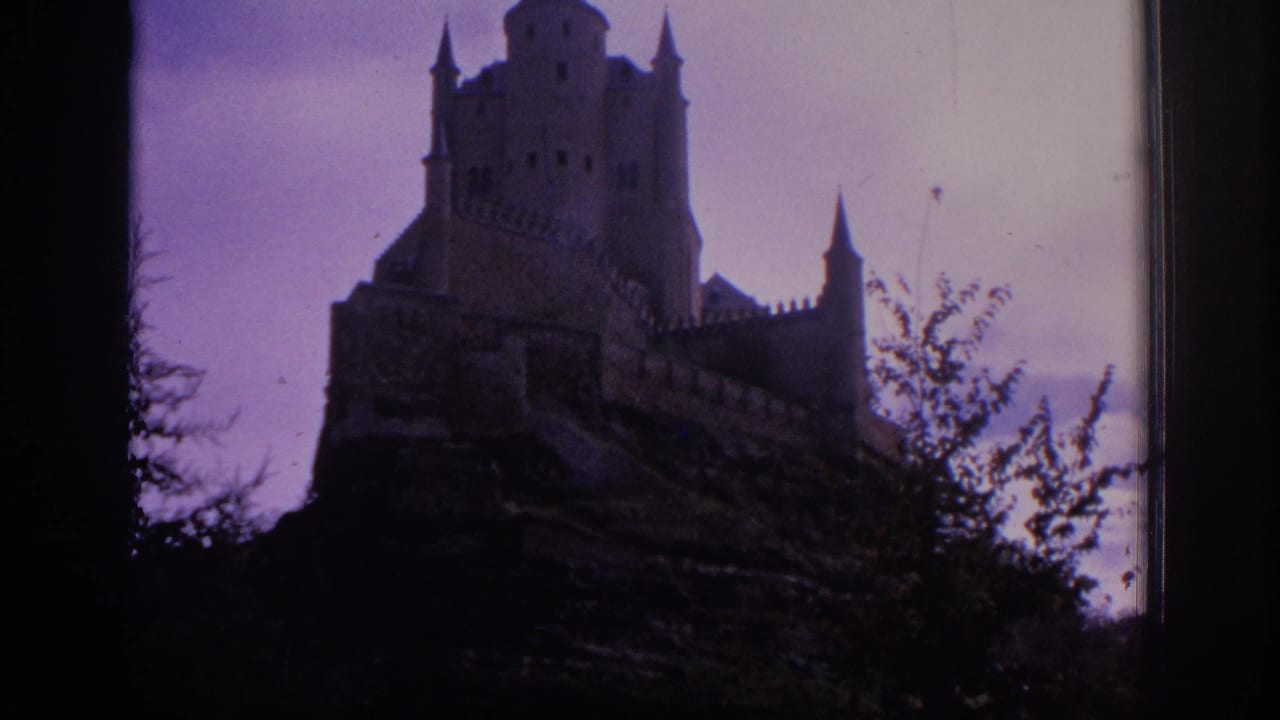 1966 Spain 8mm frame showing the Alcazar of Segovia rising above dark foreground trees under a faded purple-pink sky.