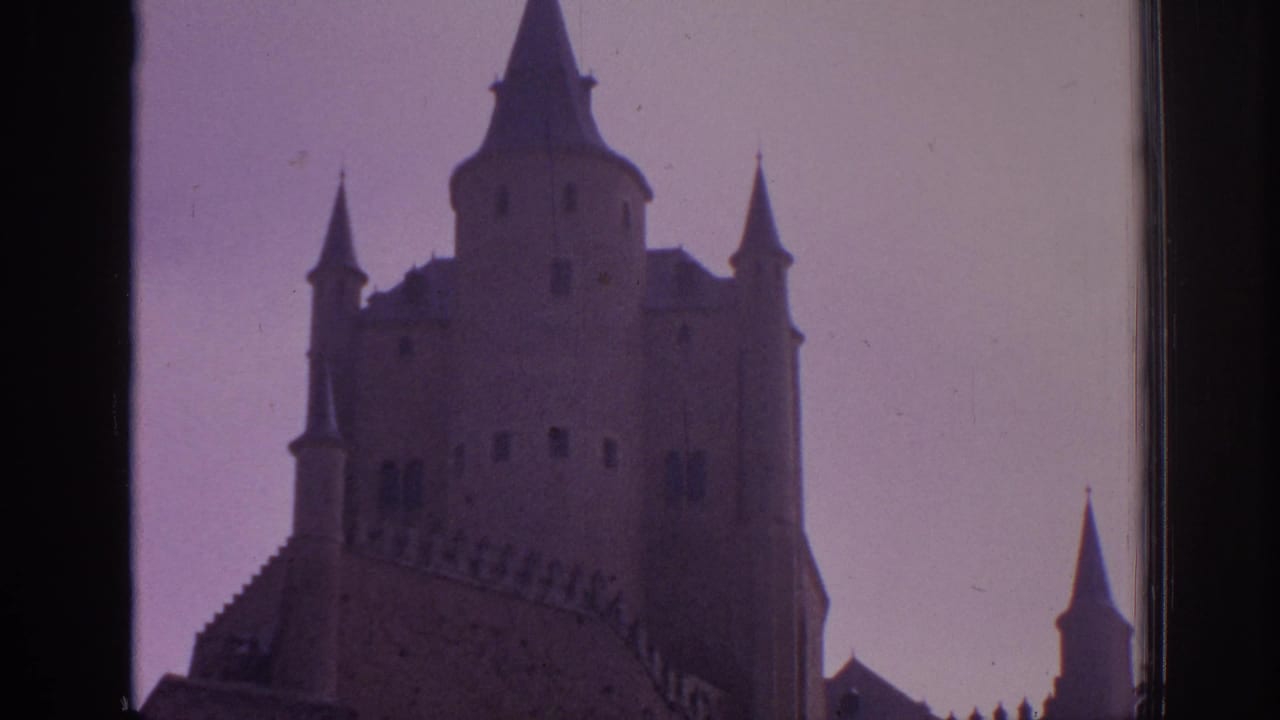 1966 Spain 8mm frame with a closer view of the Alcazar of Segovia tower, turrets, and roofline against a pink faded sky.