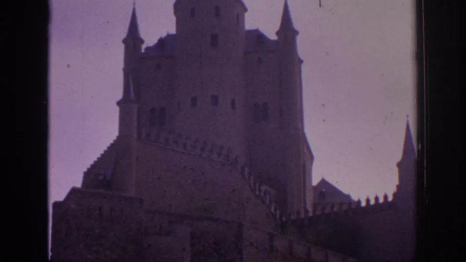 1966 Spain 8mm frame showing the Alcazar of Segovia from below, with crenellated walls, tower windows, and magenta film fading.