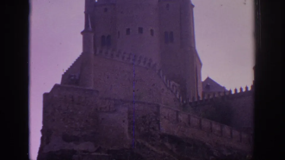 1966 Spain 8mm frame showing a close visitor-shot angle on the Alcazar of Segovia wall, tower base, and pointed turret.