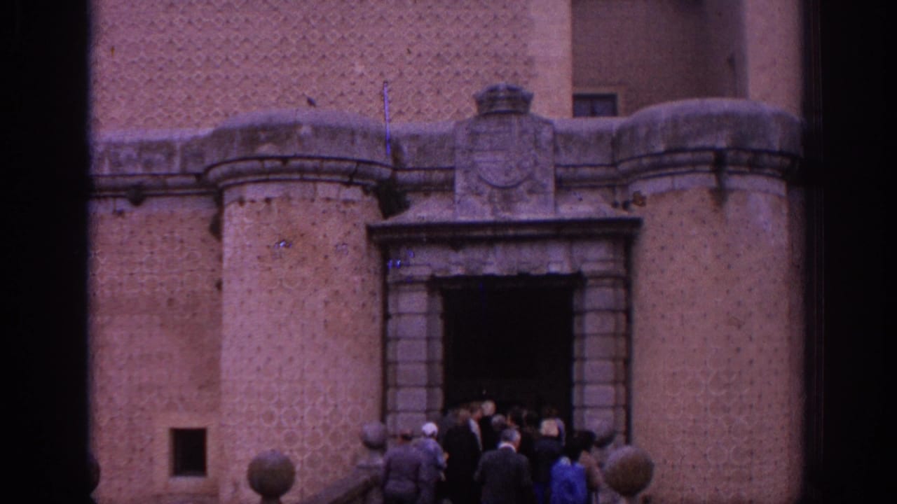 1966 Spain 8mm frame showing visitors entering a maintained castle facade with an arched stone doorway and heavy masonry.