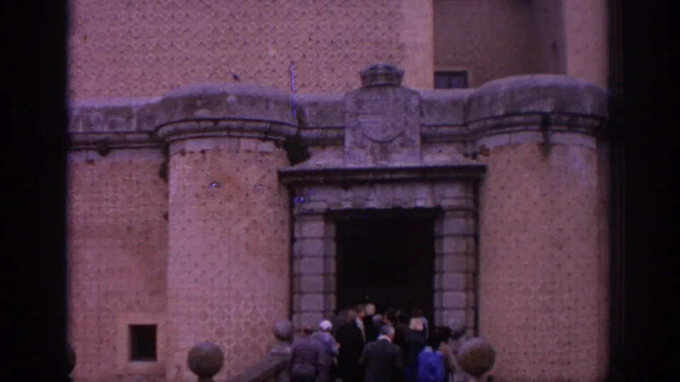 1966 Spain 8mm frame showing visitors entering a maintained castle facade with an arched stone doorway and heavy masonry.