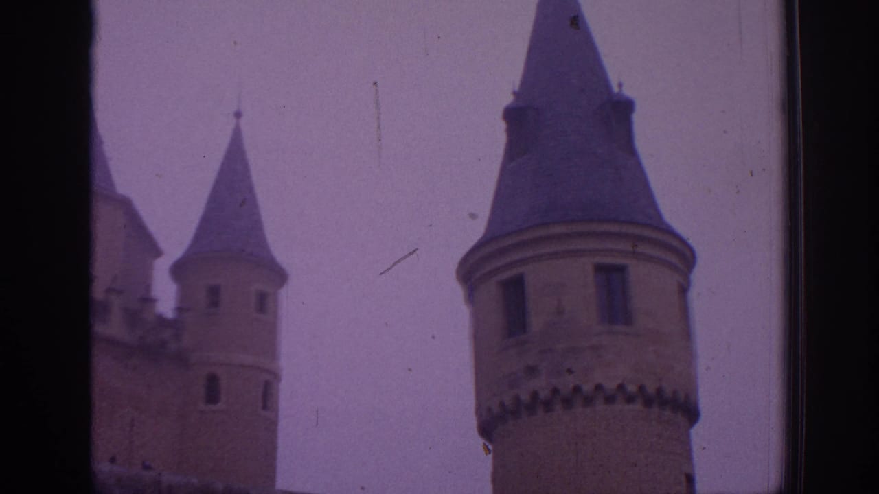 1966 Spain 8mm view of castle towers with conical roofs, narrow windows, and a hazy overcast sky.