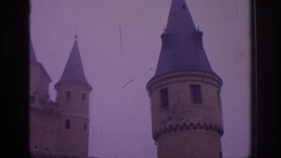 1966 Spain 8mm view of castle towers with conical roofs, narrow windows, and a hazy overcast sky.