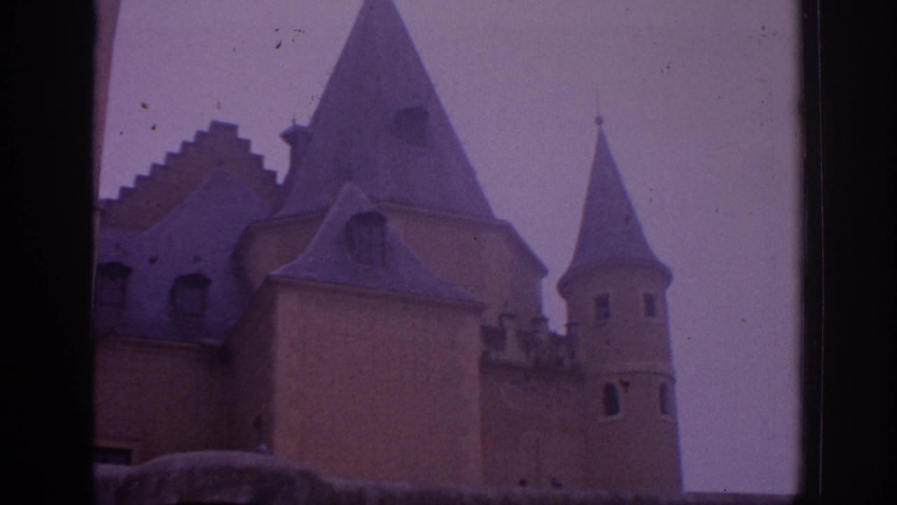 1966 Spain home-movie frame showing castle turrets, steep conical roofs, and soft purple-tinted sky.