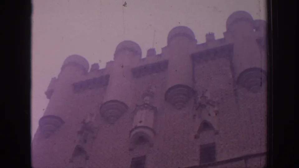 1966 Spain 8mm frame looking up at a castle facade with rounded battlements and small projecting turrets.
