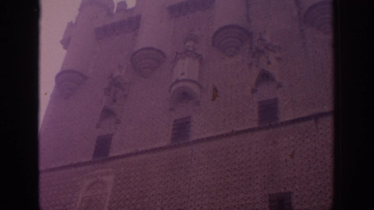 1966 Spain 8mm frame showing a historic stone building facade with rounded turrets, arched openings, and purple color shift.