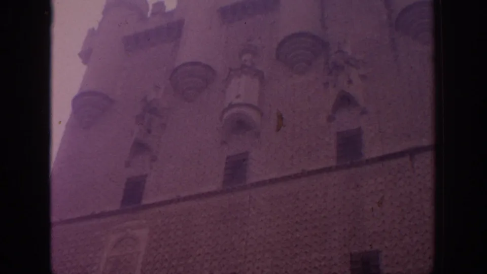 1966 Spain 8mm frame showing a historic stone building facade with rounded turrets, arched openings, and purple color shift.