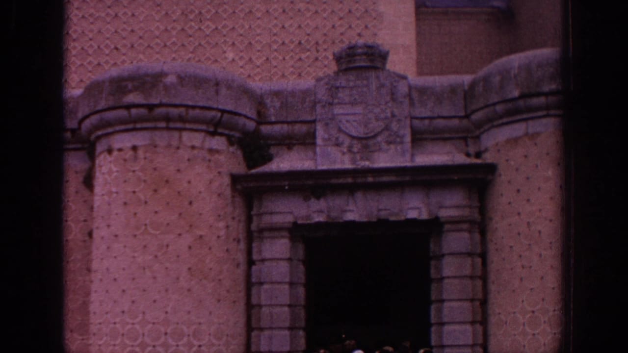 1966 Spain 8mm frame of a historic stone entrance with a dark doorway, coat of arms, rounded towers, and textured masonry.
