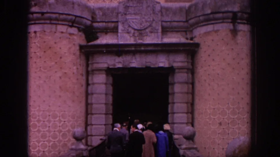 1966 Spain 8mm frame showing visitors in period clothing approaching a historic stone entrance with patterned walls and railings.