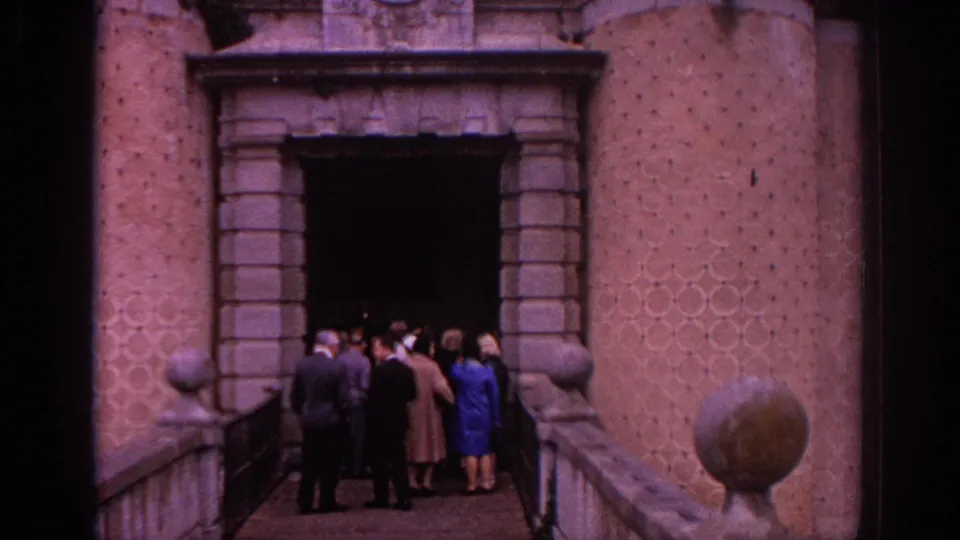 1966 Spain 8mm frame of visitors at a large stone doorway, with textured masonry, railings, and rounded architectural details visible.