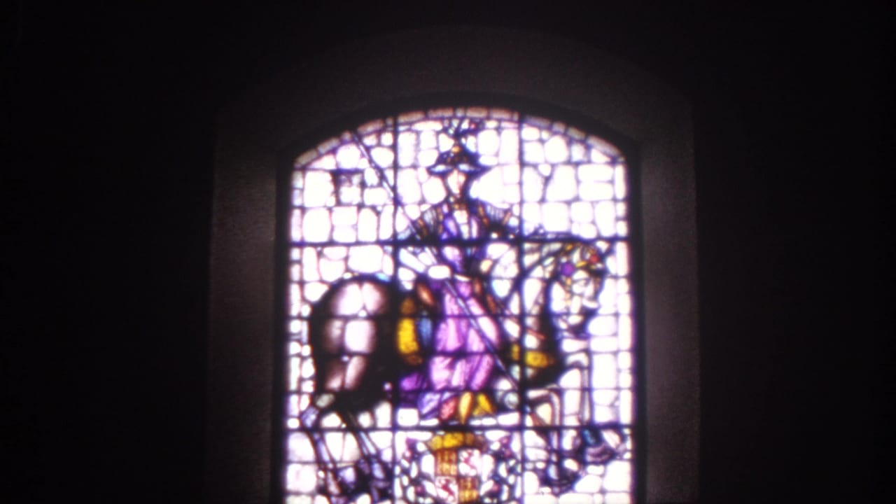 1966 Spain 8mm frame of an arched stained glass window with a horse-and-rider motif inside a dim historic interior.