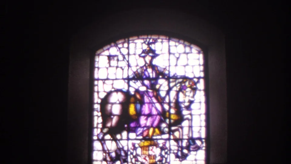 1966 Spain 8mm frame of an arched stained glass window with a horse-and-rider motif inside a dim historic interior.