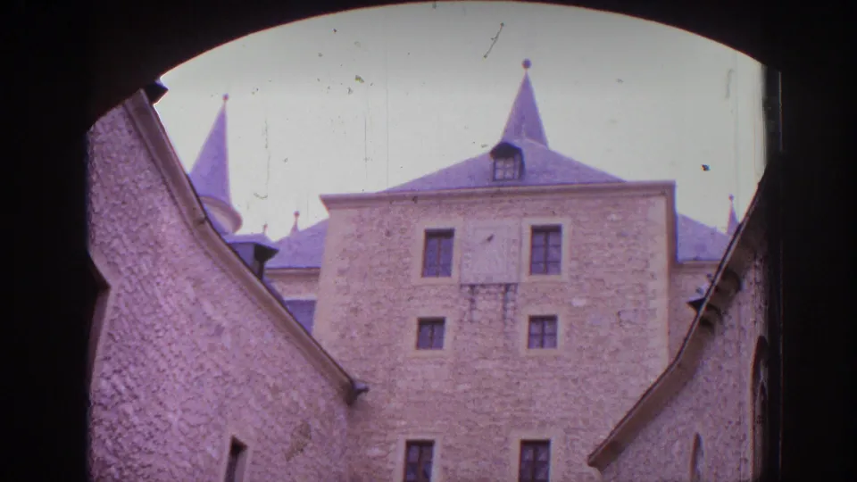 1966 Spain 8mm frame of a historic stone building with pointed roofs viewed through a shaded archway.
