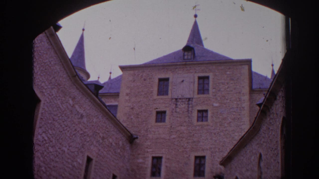 1966 Spain 8mm frame showing a stone castle facade with small windows and pointed roof spires viewed from beneath a dark arch.
