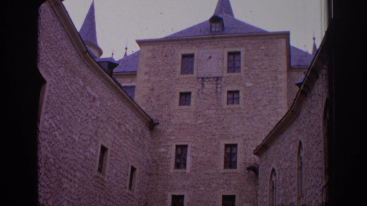 1966 Spain home-movie frame with textured stone walls, narrow windows, roof spires, and a central castle facade seen through an arch.