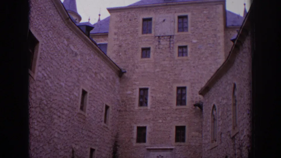 1966 Spain 8mm frame tilting lower into a stone courtyard with high walls, small windows, and an arched opening on the right.