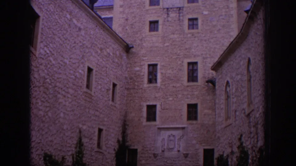 1966 Spain frame showing the lower castle courtyard facade, small windows, a doorway, masonry walls, and decorative stonework near the base.