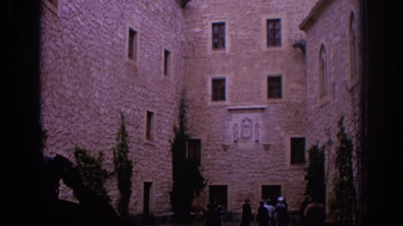 1966 Spain castle courtyard view with rough stone walls, small windows, a carved coat of arms, and distant visitors at the edge of frame.