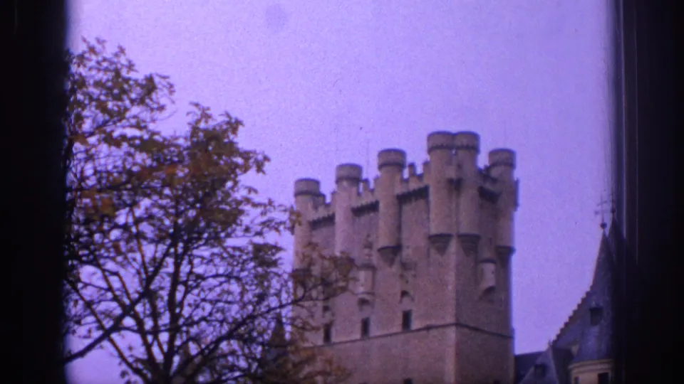 1966 Spain travel frame showing a crenellated castle tower partly framed by tree branches and rooflines under a purple-tinted sky.