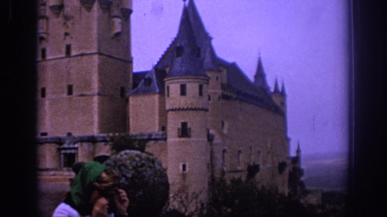 1966 Spain home-movie frame showing a woman in sunglasses and green headscarf near a large stone castle with turrets.
