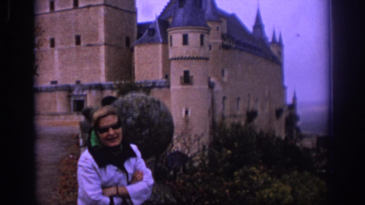 Woman in sunglasses stands before the Alcazar of Segovia with castle towers behind her.