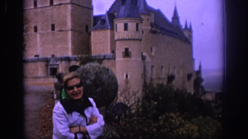 1966 Spain home-movie frame showing a woman in a white jacket posing in front of the Alcazar of Segovia.