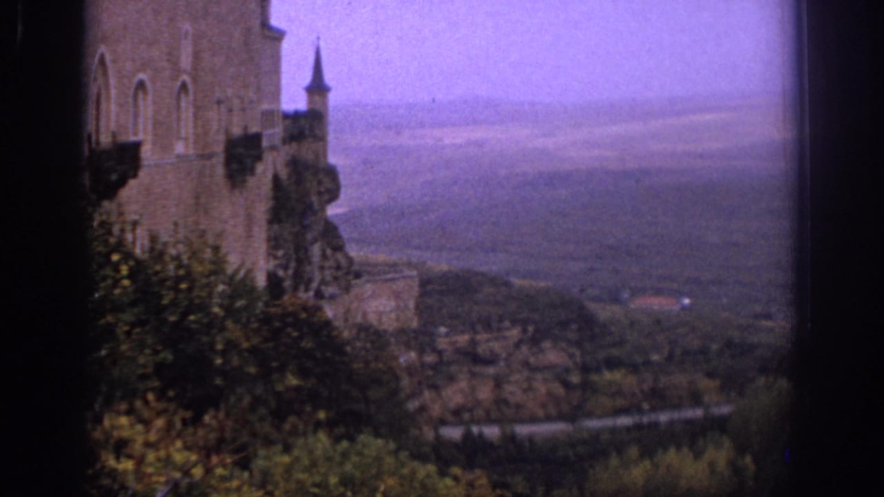 Castle wall and turret stand above a rocky slope and broad valley.