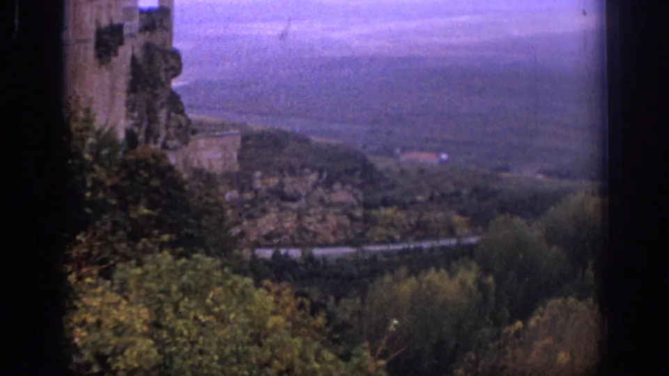 1966 Spain home-movie frame showing the Alcazar of Segovia above a green valley and road.