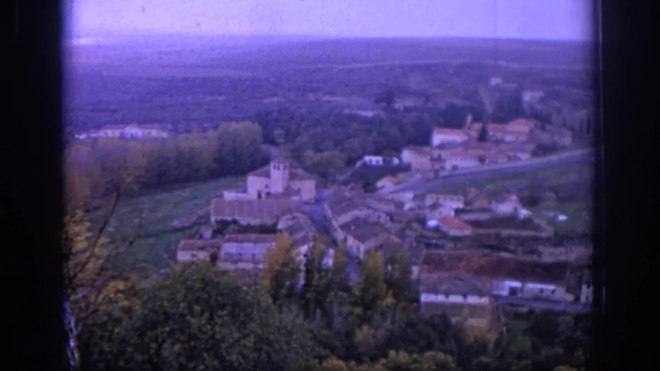1966 Spain 8mm frame showing a hillside village cluster with a tower, roads, trees, and open countryside beyond.