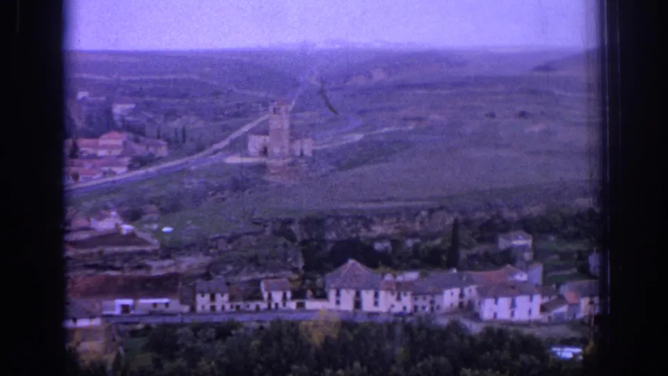 1966 Spain 8mm view of a road, village rooftops, open fields, and a castle-like structure on the hillside.